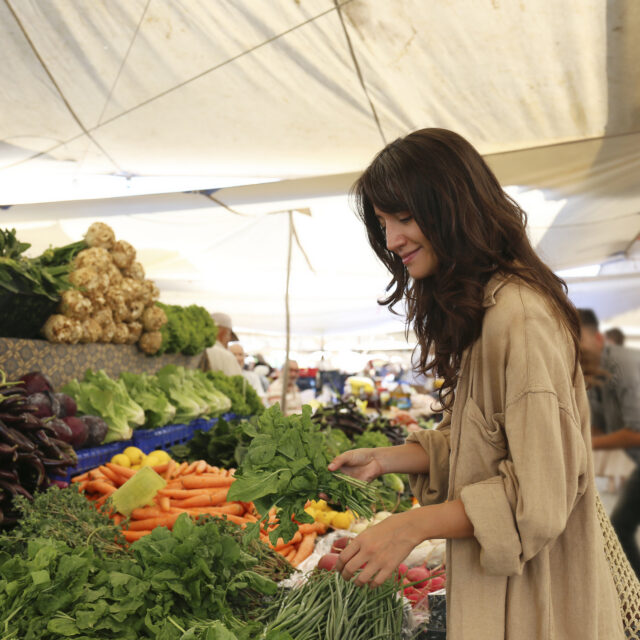 Young woman choosing fruits, vegetables, herbs and greens from a stand on farmers market. Shopping for organic local produce. Close up, copy space, background.